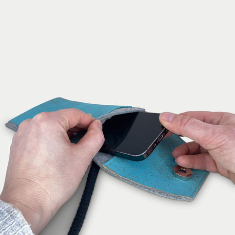 Person, die ein Samsung Galaxy A17 in eine stilvolle hellgraue und blaue Filztasche mit Schulterriemen steckt.