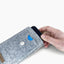 Ein Motorola Edge 50 neo wird von Hand aus einer stilvollen hellgrauen Handytasche mit Knopfverschluss gezogen.